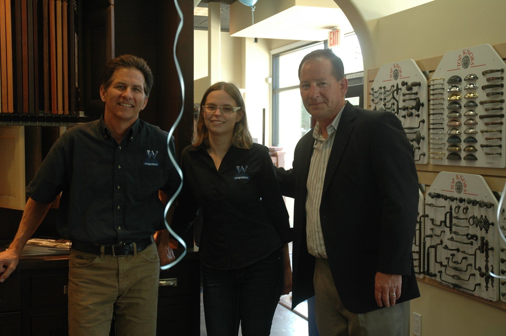 Three people smiling in a hallway, standing beside a display of tools and equipment.