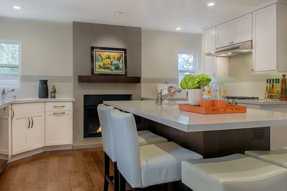Modern kitchen with island, white cabinets, and fireplace in the background