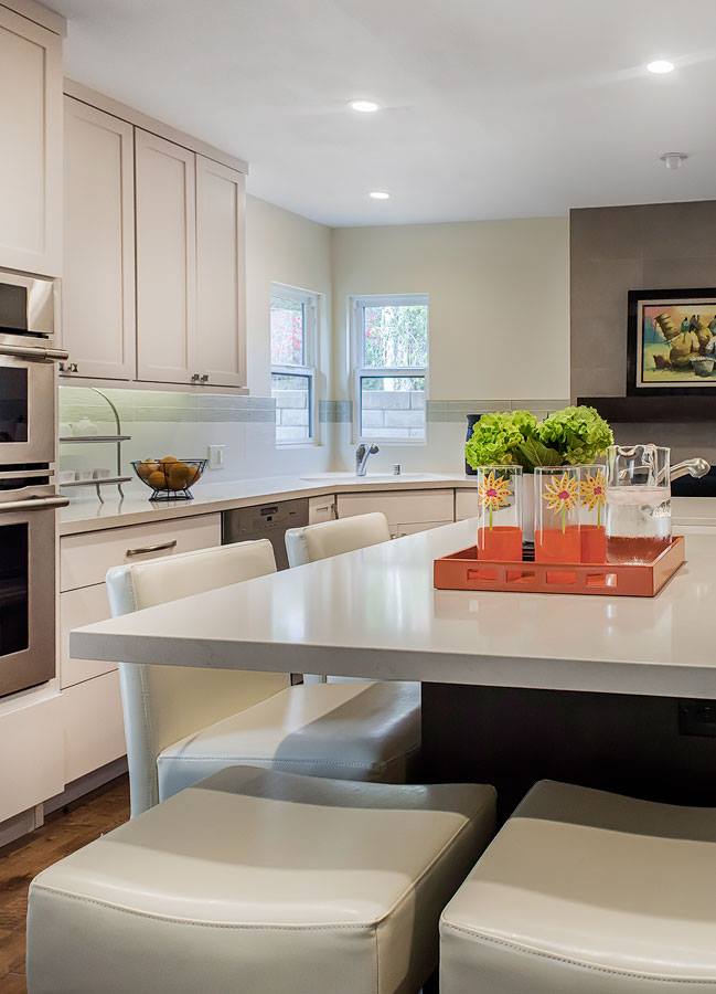 Bright modern kitchen with white cabinetry, island stools, and a tray of orange drinks and green plants