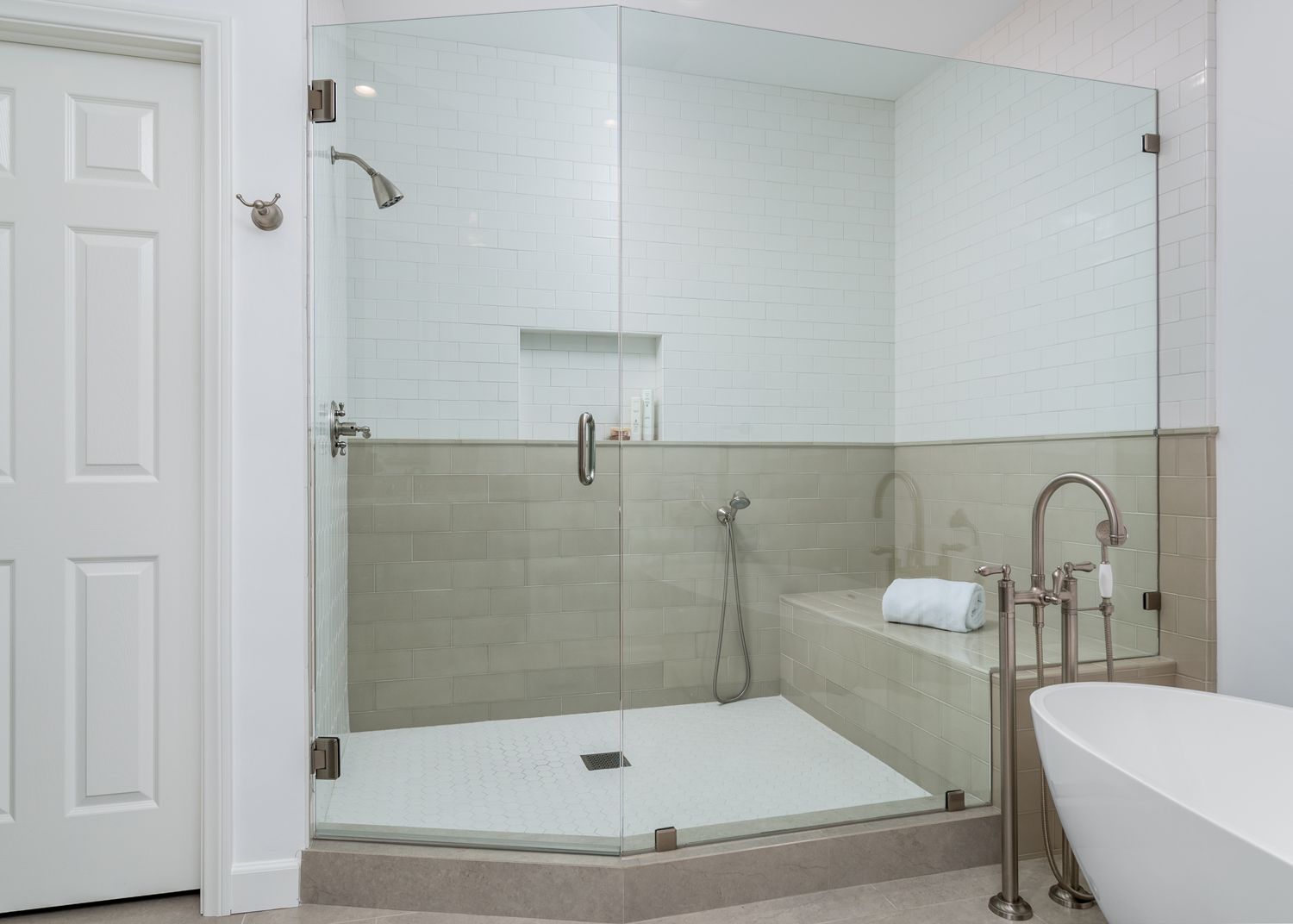 Modern tiled bathroom with glass walk-in shower, built-in bench, and partial bathtub view