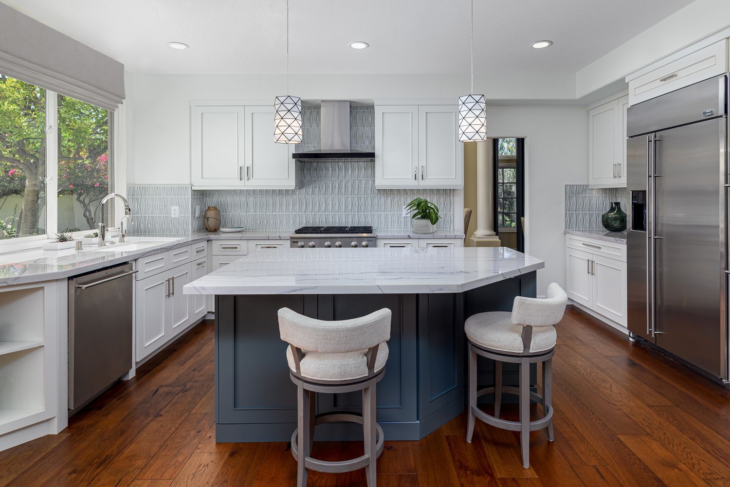 Bright modern kitchen with white cabinets, marble island, wood floors, and two stools