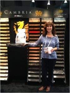 Woman stands smiling by a Cambria display, holding a drink in a showroom.