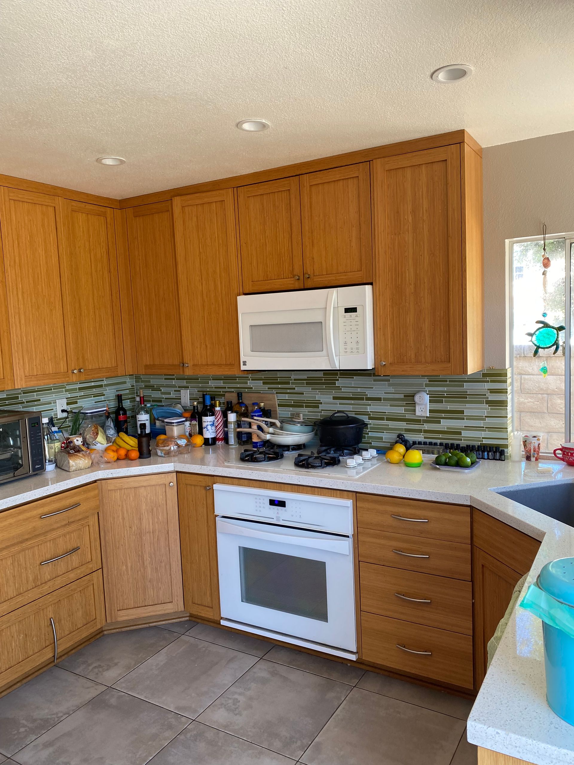 Kitchen with wood cabinets, white appliances, tiled floor, and cluttered countertops.