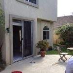 Patio outside a beige house with open sliding door, potted plant, and a small folding chair