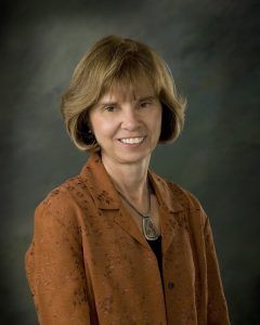 Portrait of a smiling woman in a brown jacket against a dark studio background