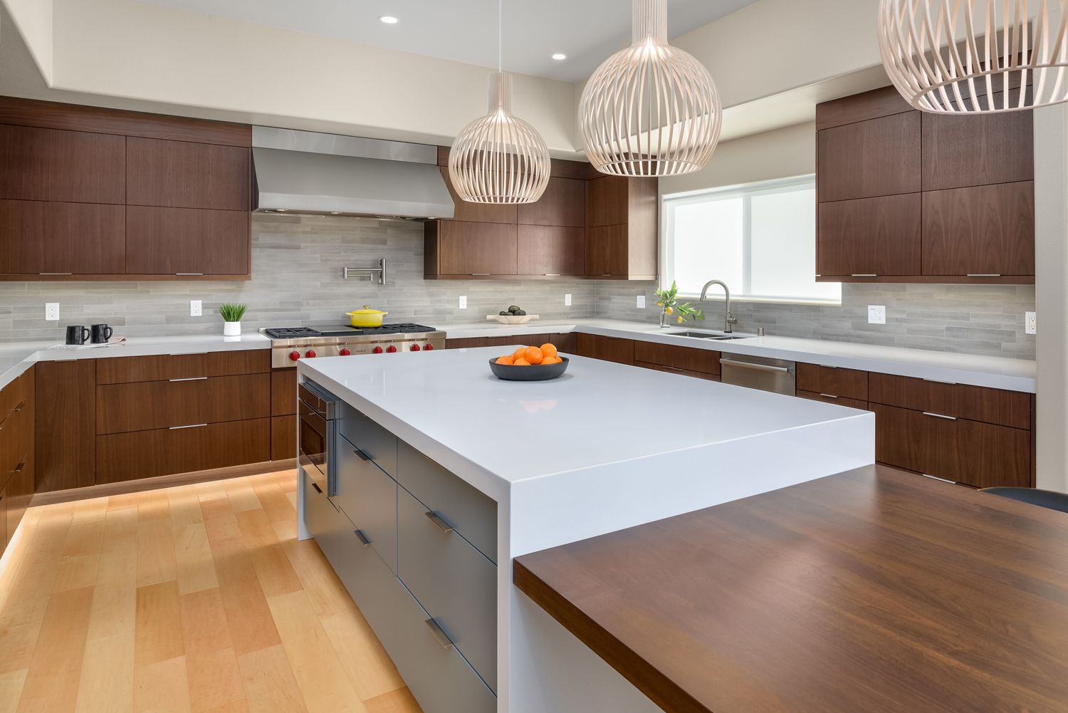 Modern kitchen with a large white island, dark wood cabinets, pendant lights, and a window over the sink