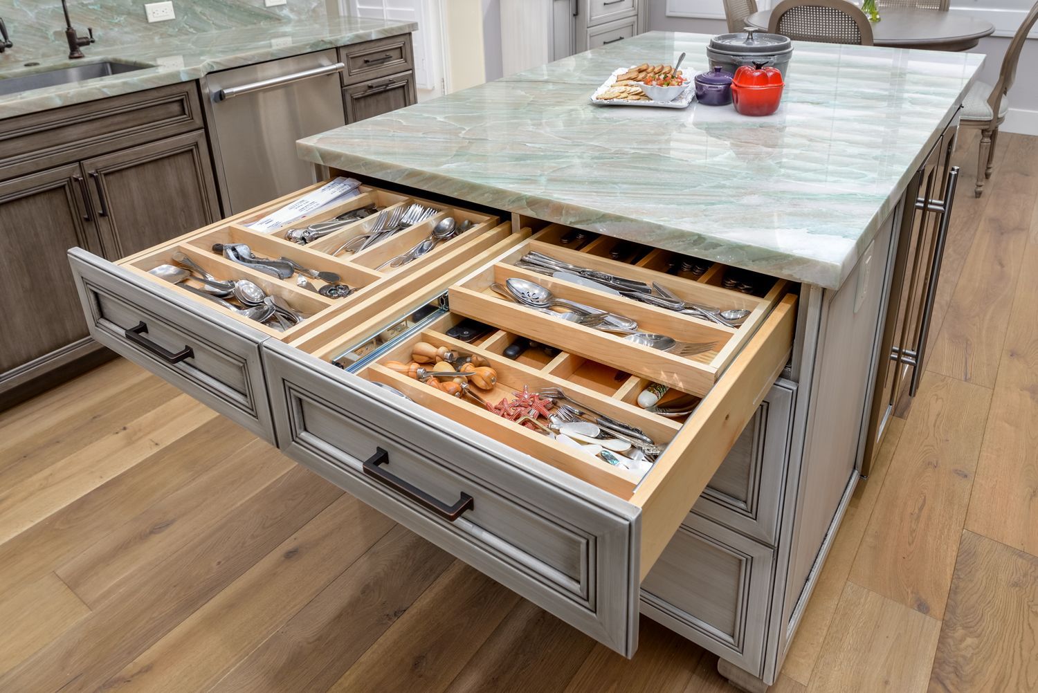 Kitchen island with three open drawers holding utensils and a marble countertop with bowls and fruit.