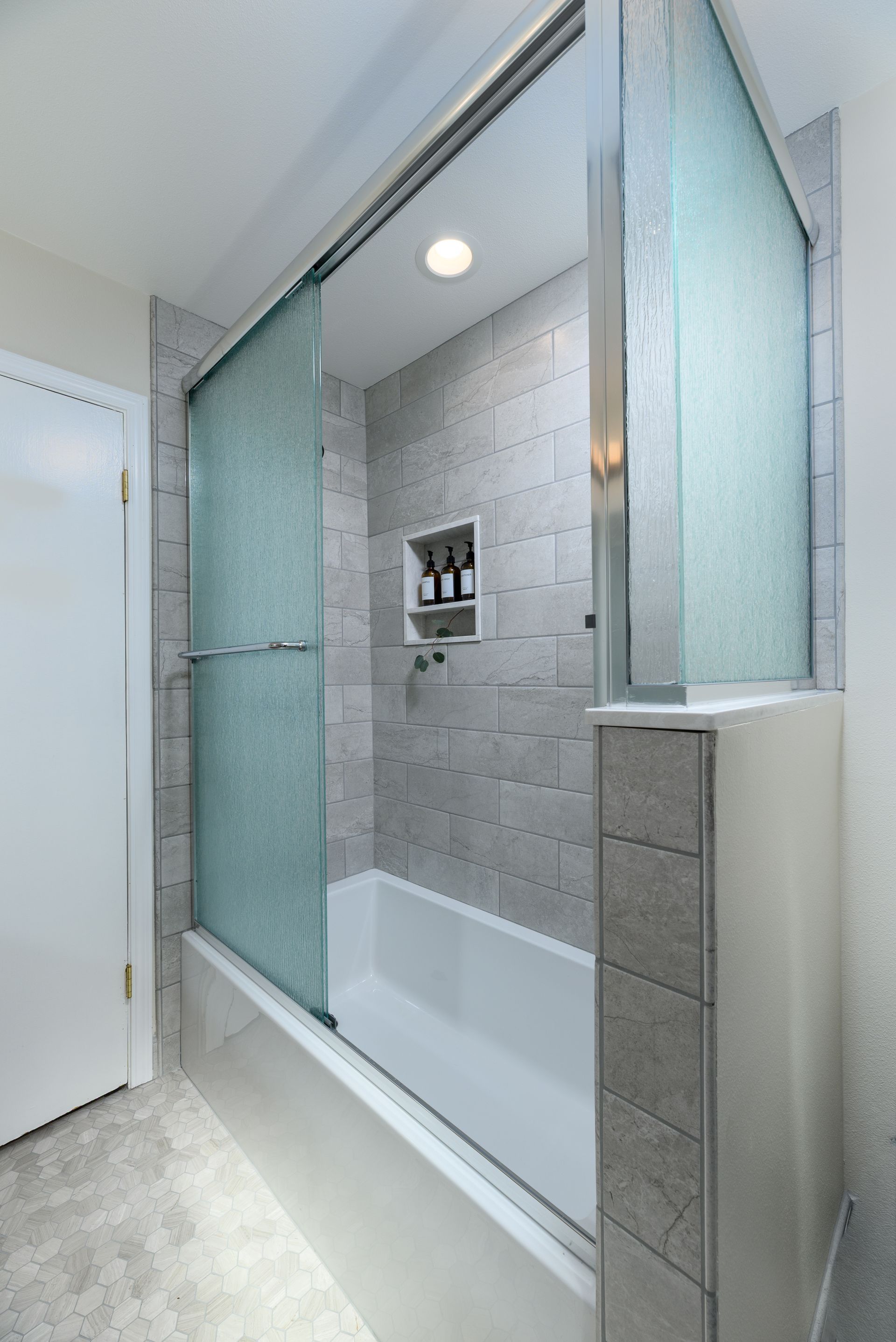Modern bathroom shower with frosted glass panels, gray tile walls, and a built-in shelf.