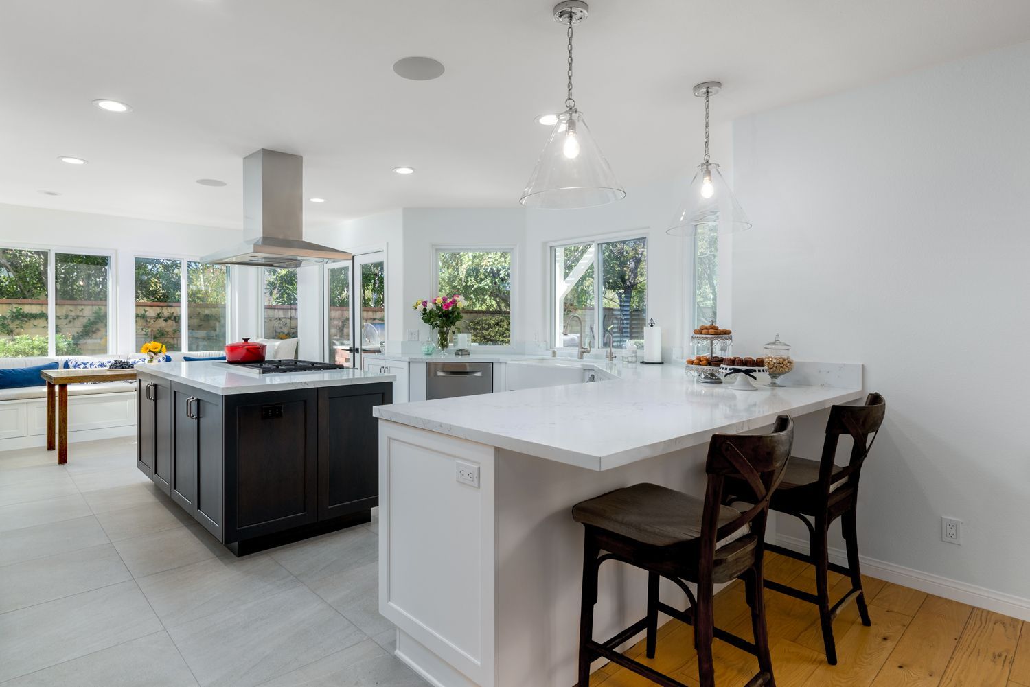 Bright modern kitchen with white island, dark stools, pendant lights, and large windows