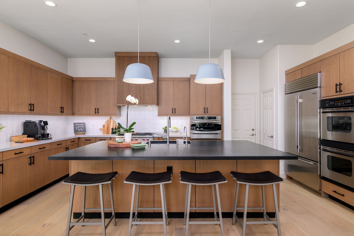 Modern kitchen with island, wooden cabinets, black countertops, and pendant lights