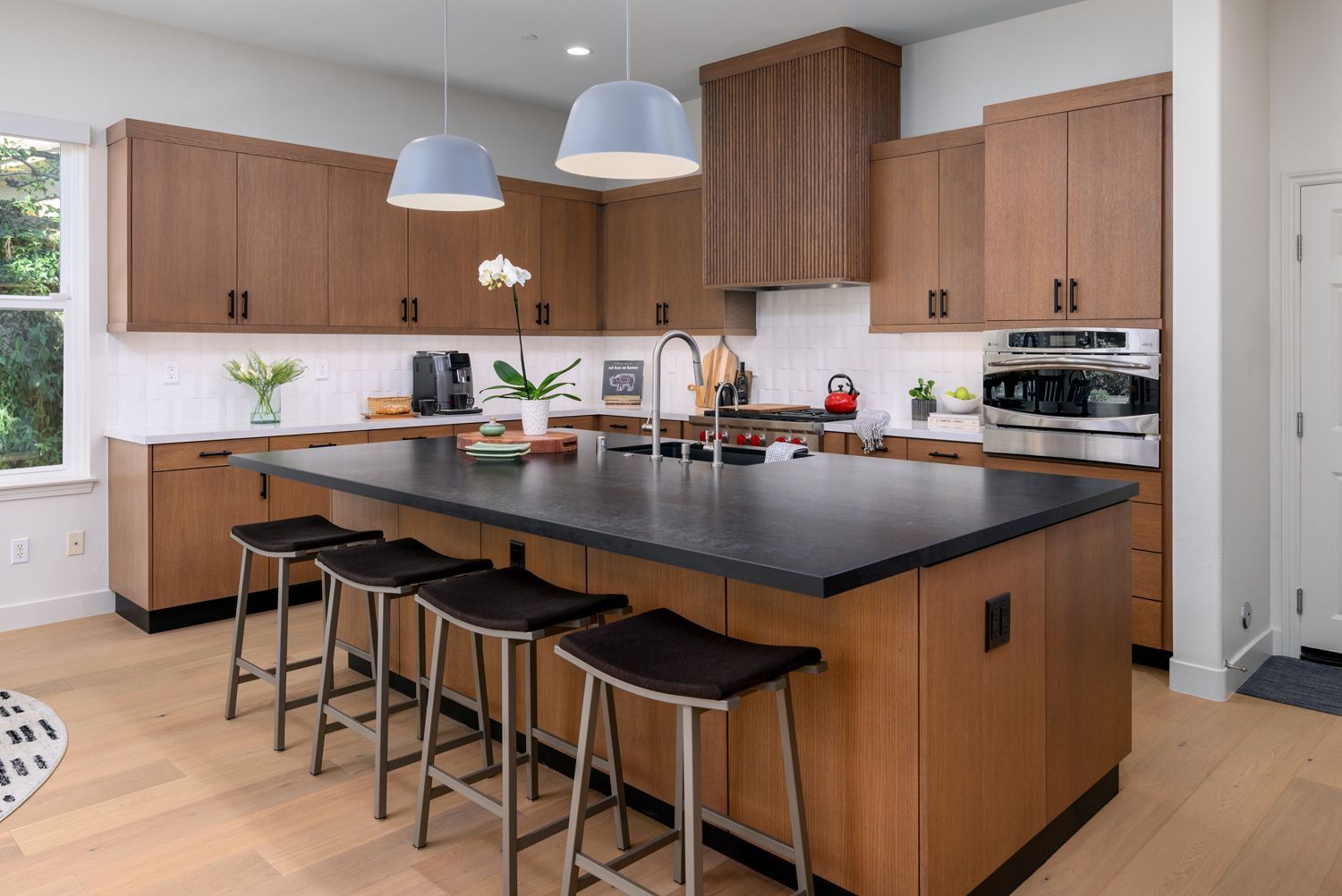 Modern kitchen with large black island, wooden cabinets, pendant lights, and bar stools