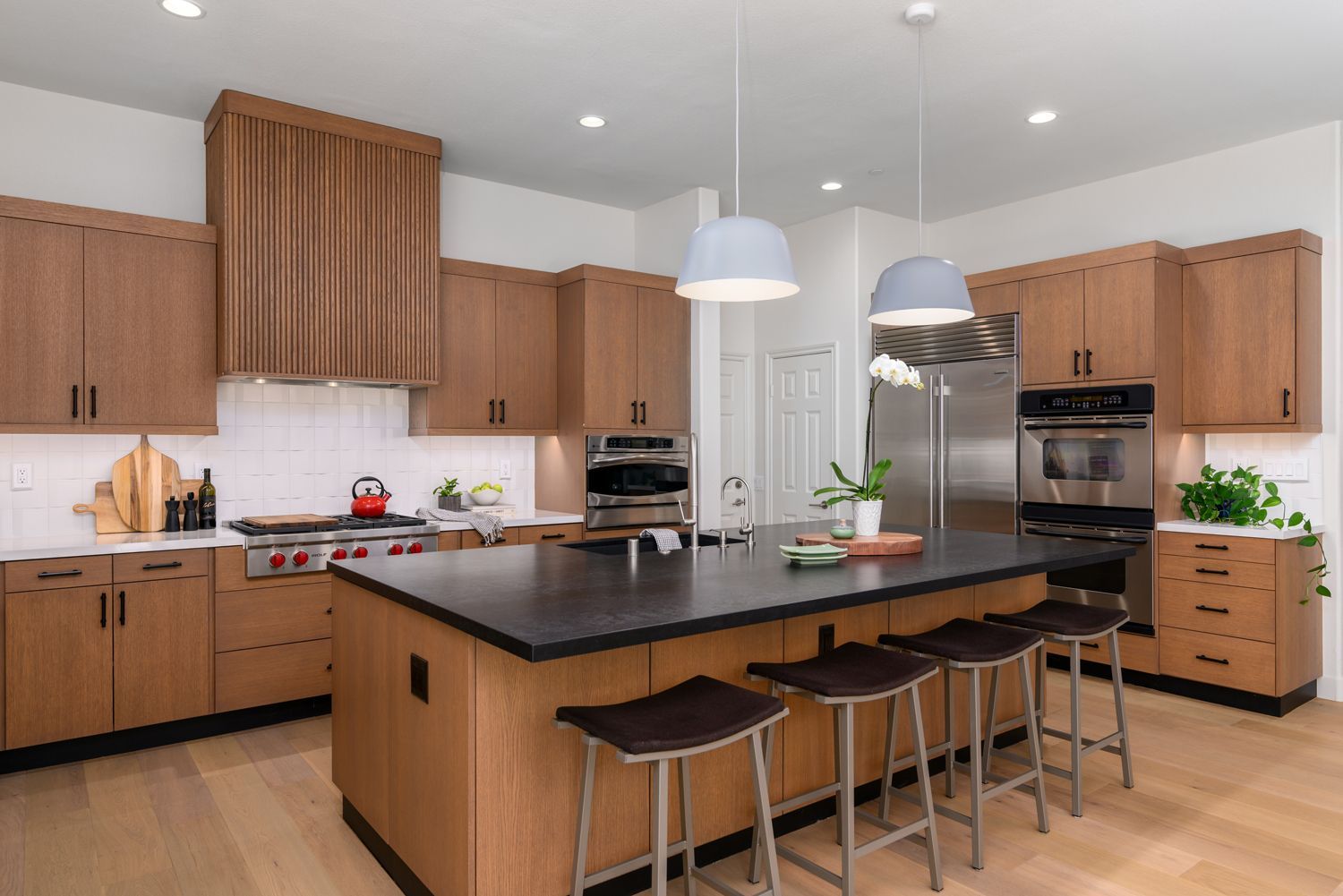 Modern kitchen with wood cabinets, black island countertop, stools, and pendant lights