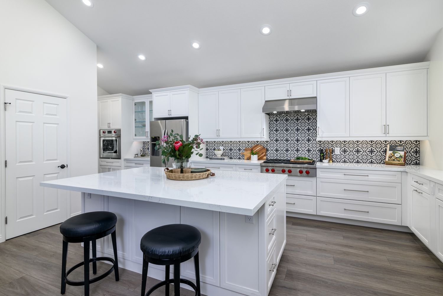 Bright modern white kitchen with island, black stools, and patterned backsplash