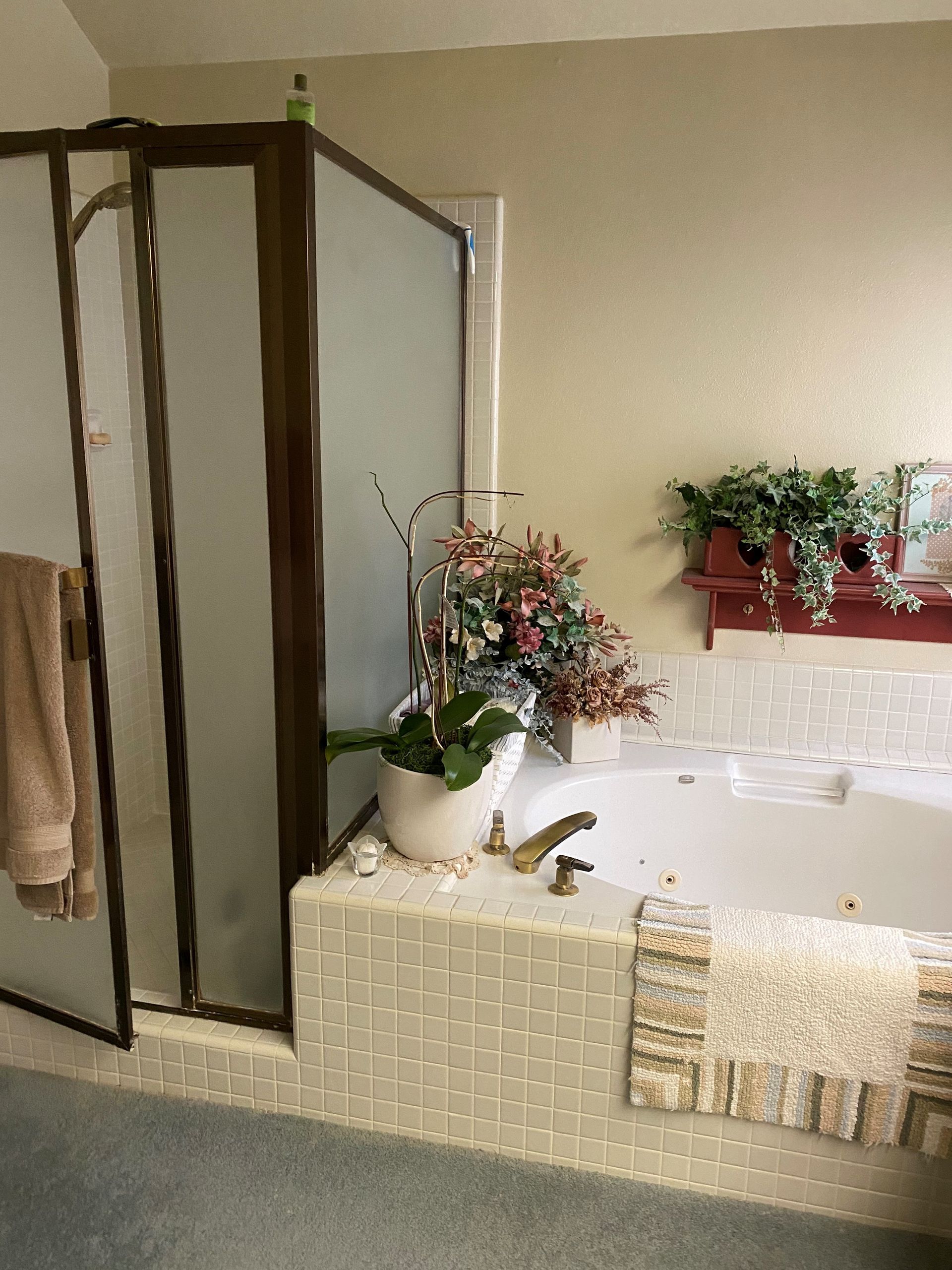 Bathroom with a glass shower, tiled jacuzzi tub, and floral arrangements on the vanity and tub ledge