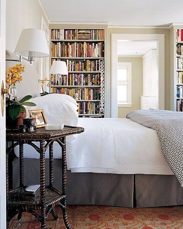 Cozy bedroom with a white bed, bookshelves, lamps, and a doorway to a bright room