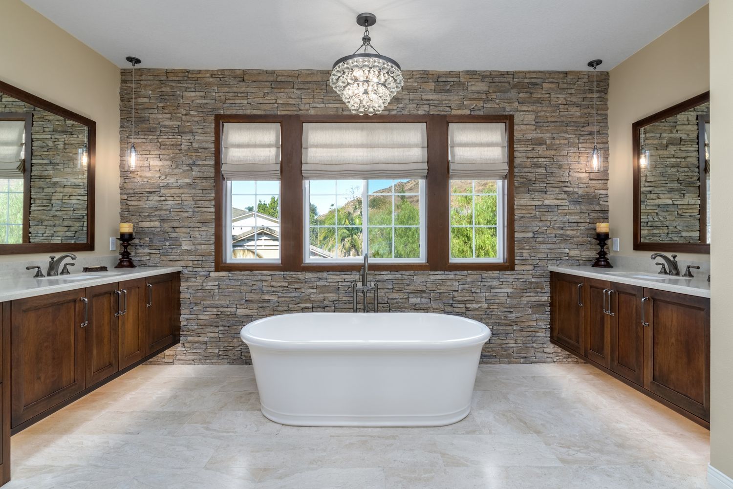 Modern bathroom with a freestanding tub, stone accent wall, wood vanities, and large windows
