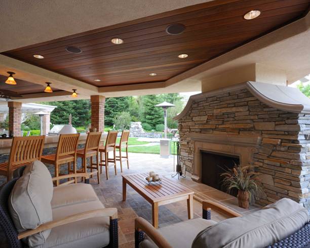 Covered patio with stone fireplace, wooden ceiling, and outdoor seating overlooking a green yard