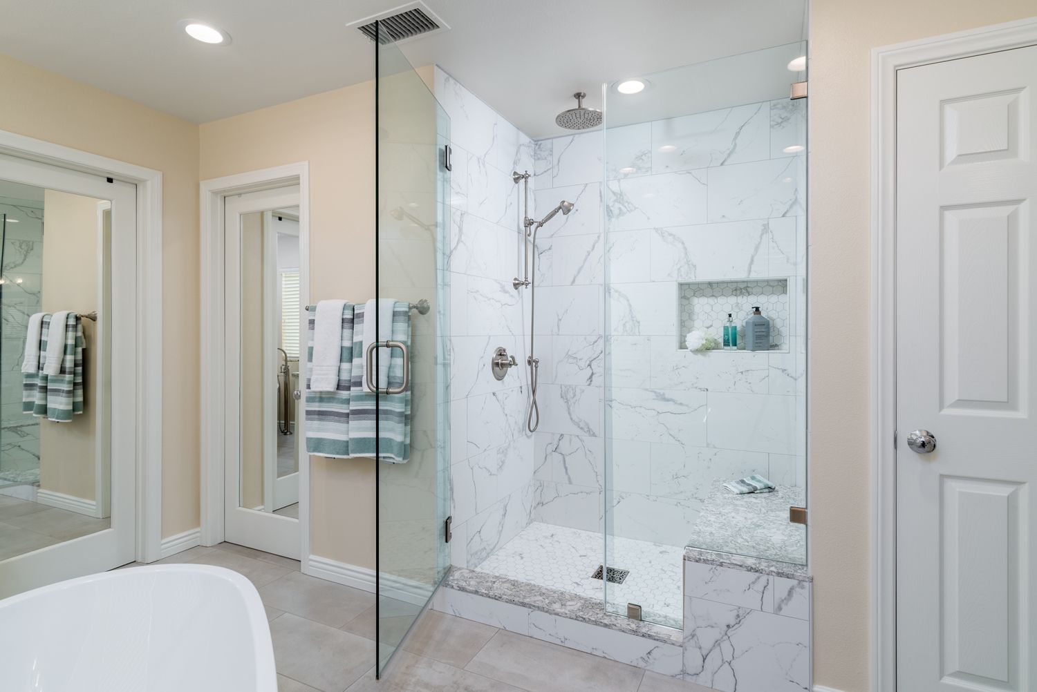 Bright bathroom with a glass walk-in shower, marble tile walls, and mirrored vanities.