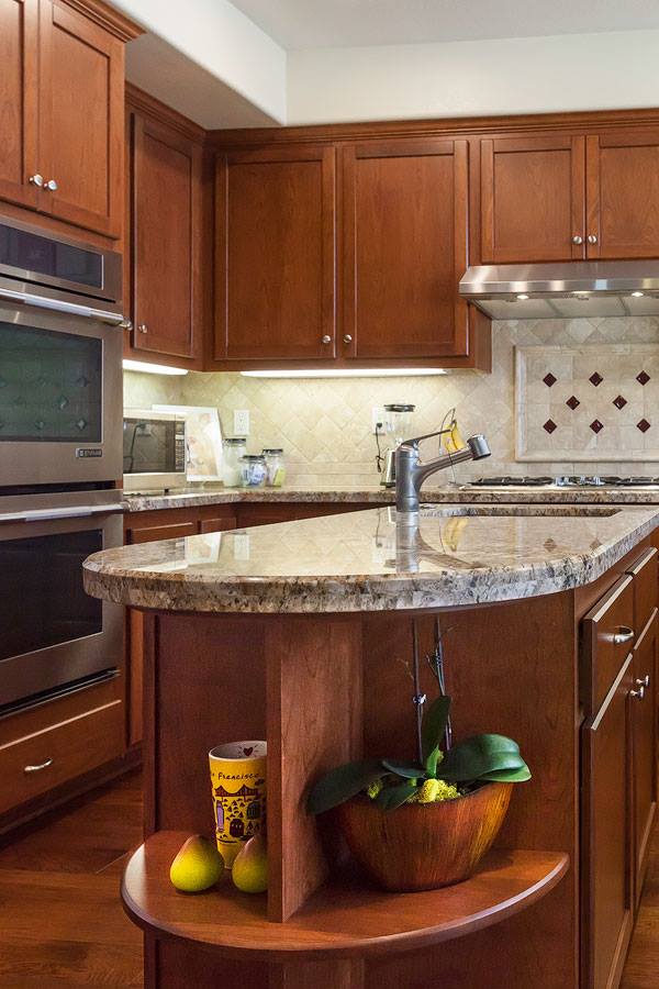 Modern kitchen with cherry cabinets, granite island, sink, and a small fruit bowl on a curved shelf