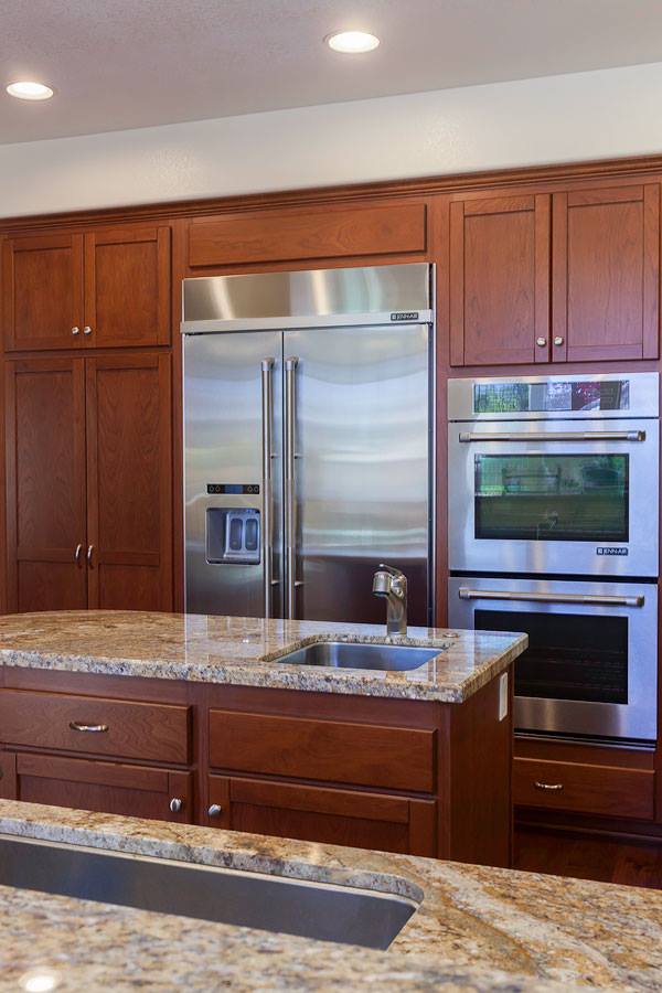 Modern kitchen with stainless steel refrigerator, double oven, wooden cabinets, and granite island countertop