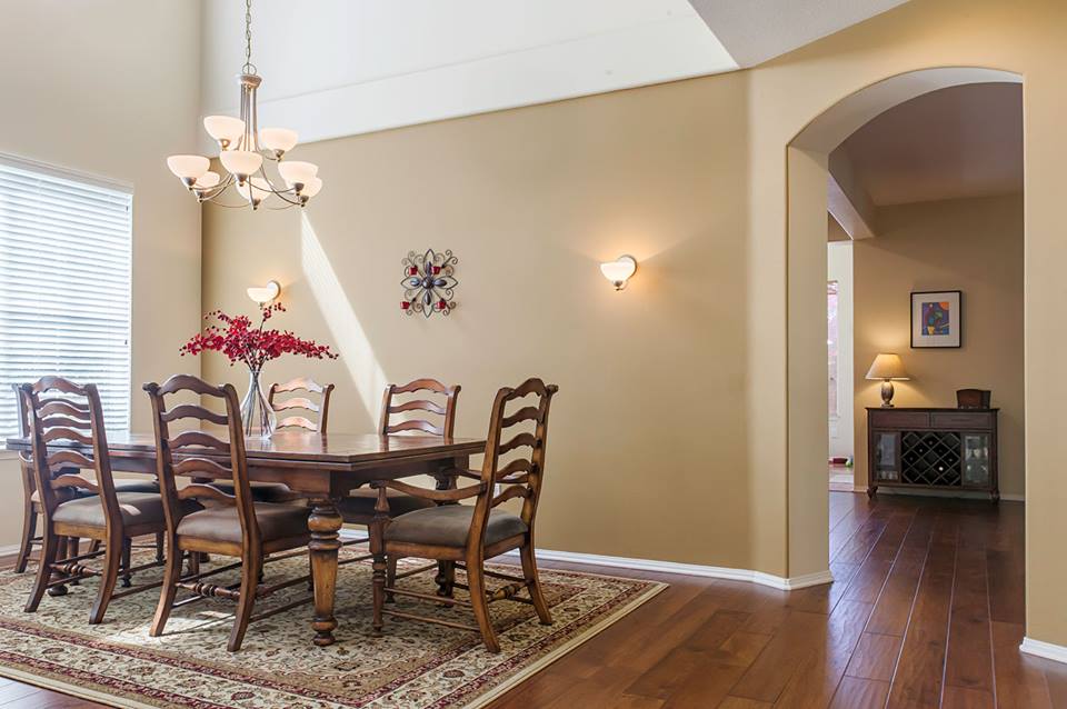 Dining room with wooden table and chairs, chandelier, beige walls, and arched entry to hallway.