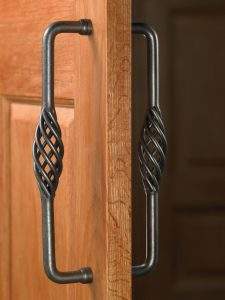 Close-up of two black metal cabinet handles on a wooden door, with one handle open and one reflected behind it