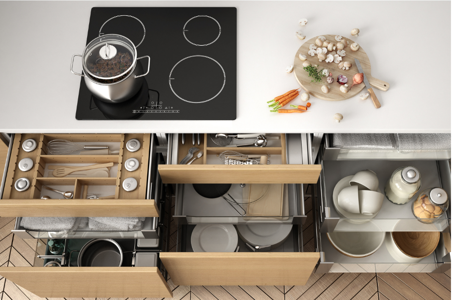 Top-down view of a modern kitchen counter and open drawers with cookware, dishes, and utensils organized inside.