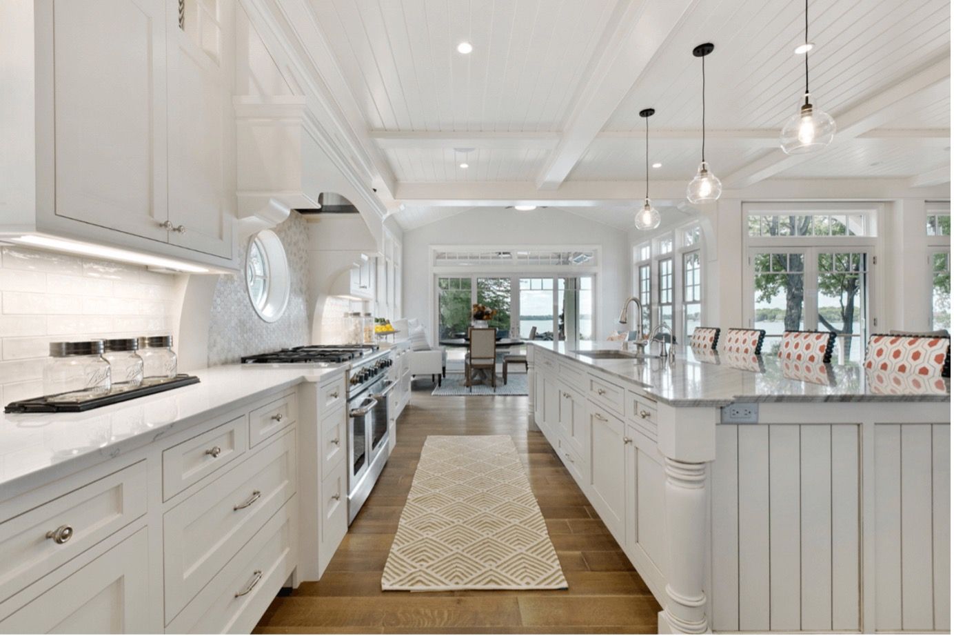 Bright white farmhouse kitchen with long island, pendant lights, and patterned runner on wooden floor