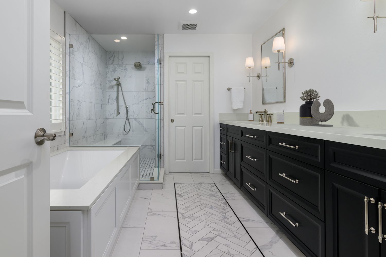 Modern white bathroom with black vanity, freestanding tub, and glass-enclosed shower