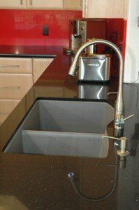 Modern kitchen with black countertop, gray sink, and tall chrome faucet before red backsplash