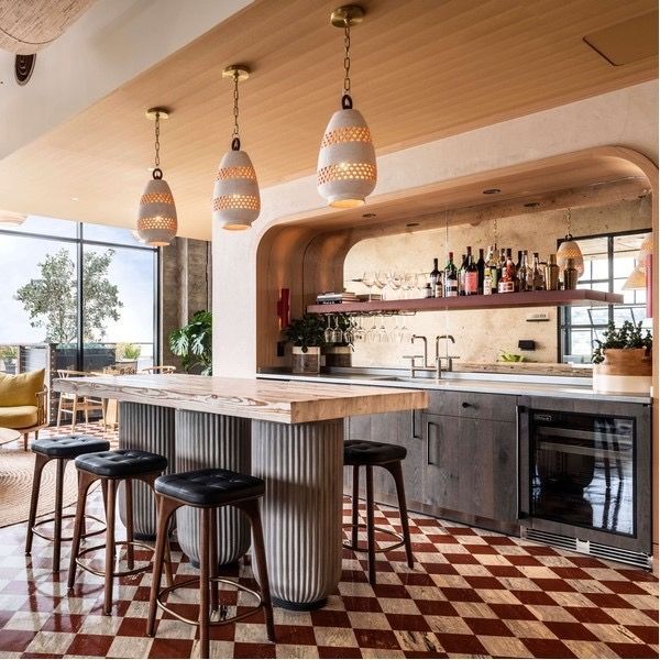 Modern coastal bar with striped pendant lights, wooden counter stools, and red-and-white checkered floor