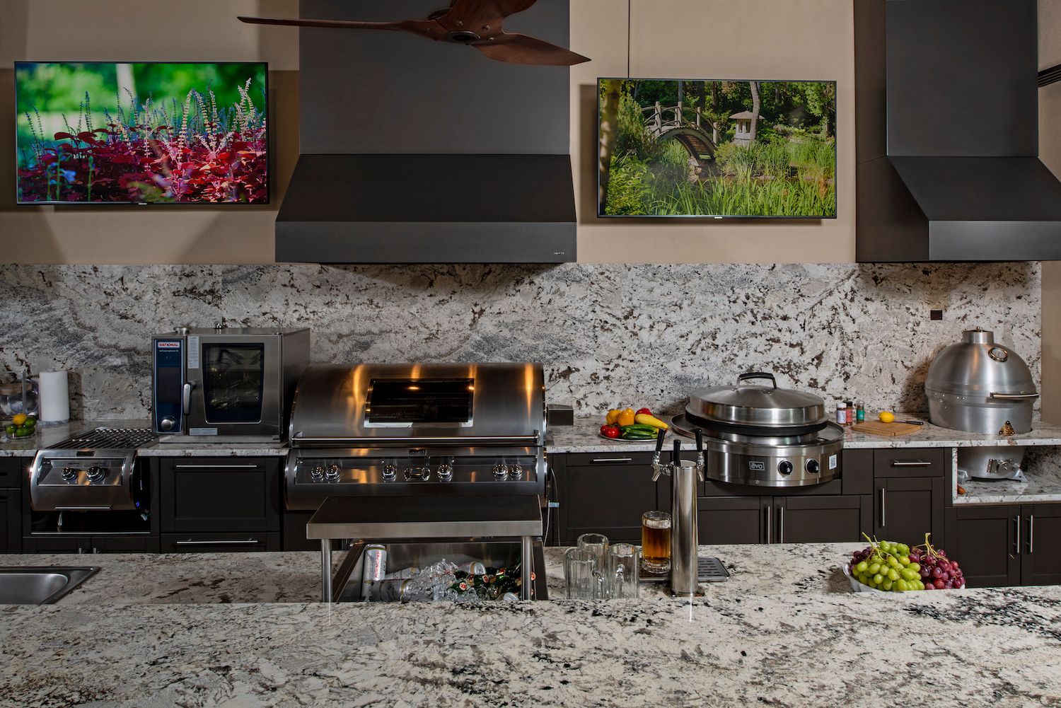 Modern kitchen with speckled granite counters, stainless appliances, pots, and two wall-mounted TVs behind the stove