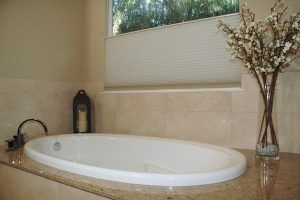 Bathroom with a built-in bathtub, beige tile, a window shade, and a vase of branches on the counter