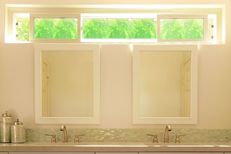 Bathroom vanity with two mirrors, twin sinks, and a bright window above