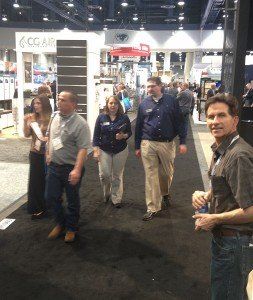 People walking through a crowded indoor trade show with booths and display shelves in the background