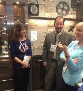 Three people chatting in a lobby, standing near a wall with clocks and decorative circles.