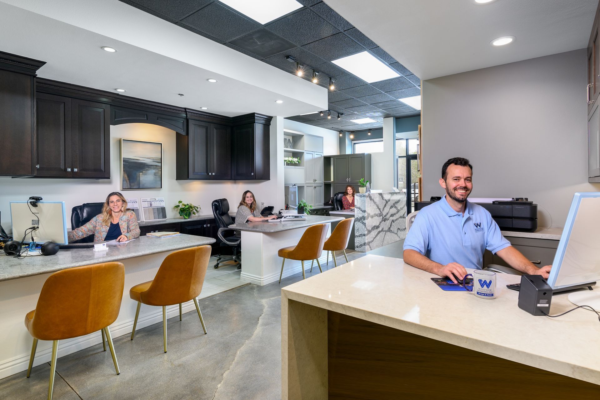 Modern office reception area with people working at desks and a smiling man at the front desk