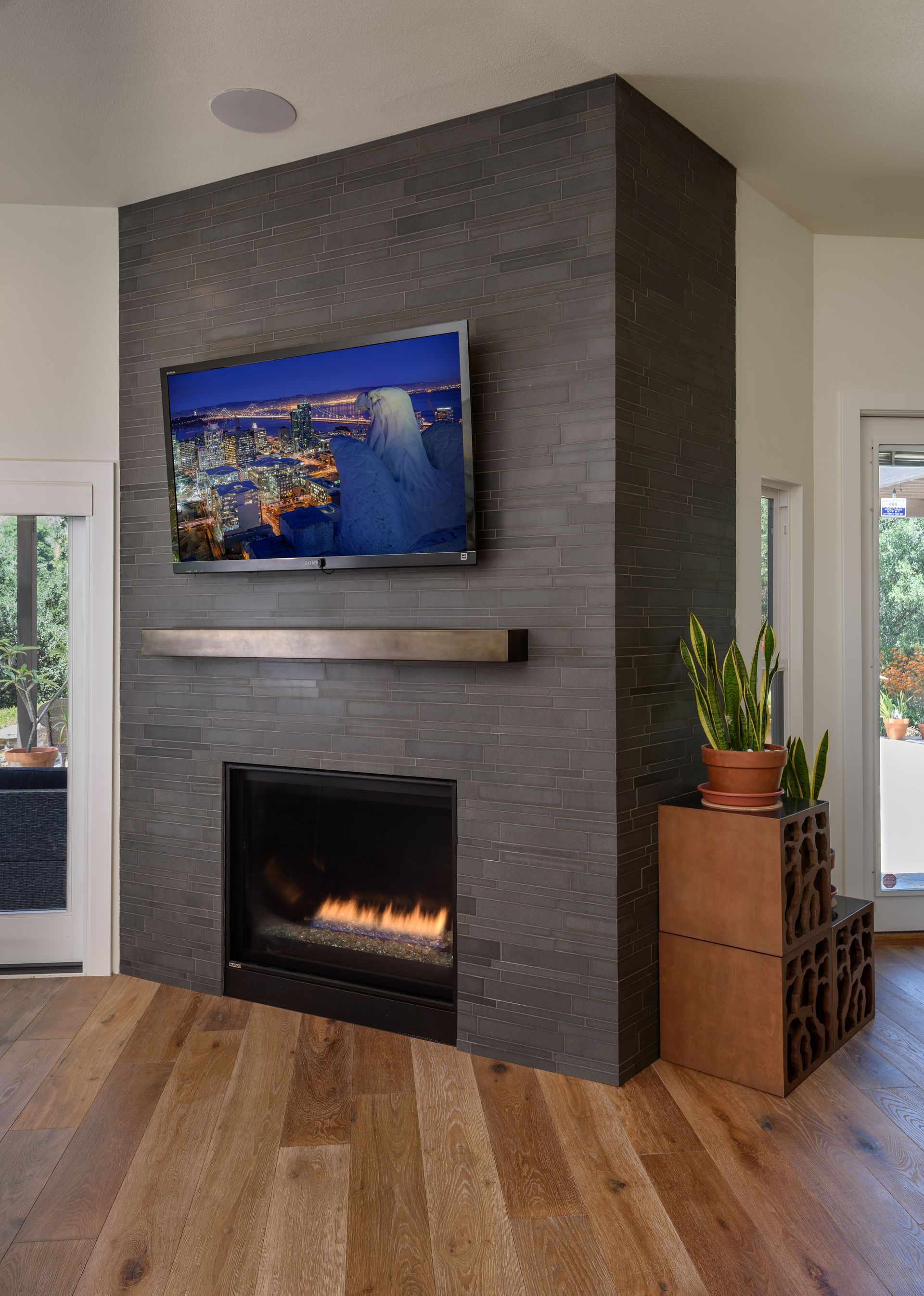 Modern living room with dark tiled fireplace, wall-mounted TV, and wood floors