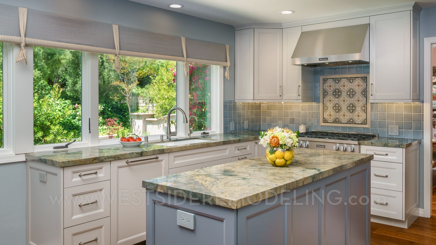 Bright blue kitchen with marble island, white cabinets, and large window overlooking greenery