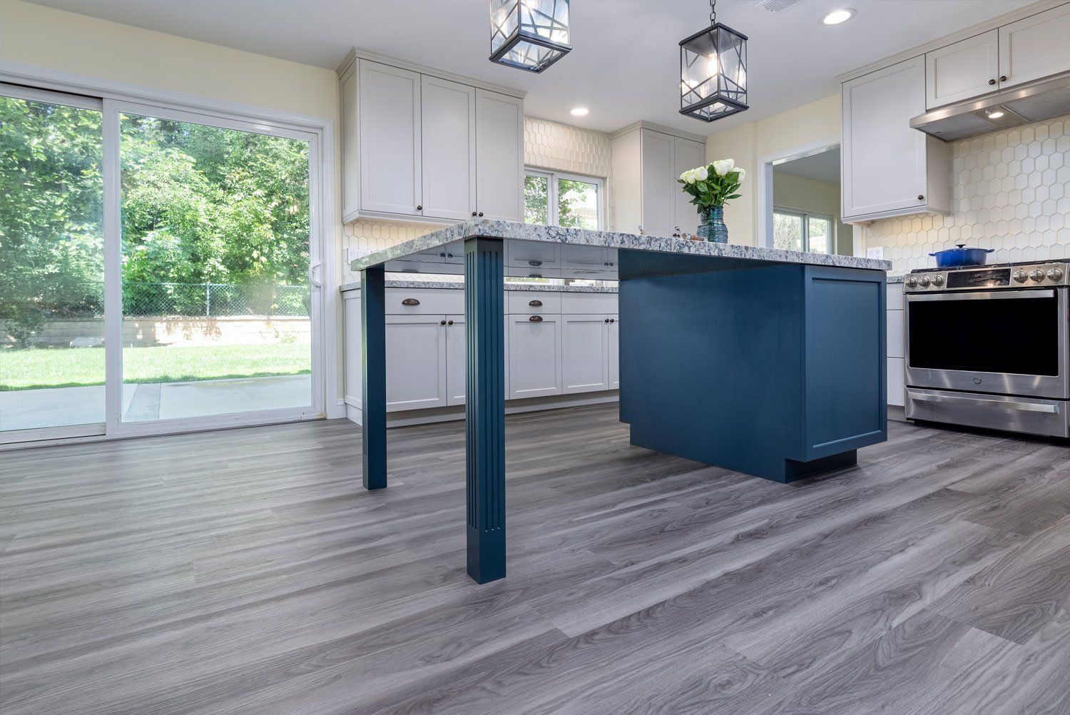 Modern kitchen with navy island, stainless appliances, gray floors, and sliding glass doors to a green yard