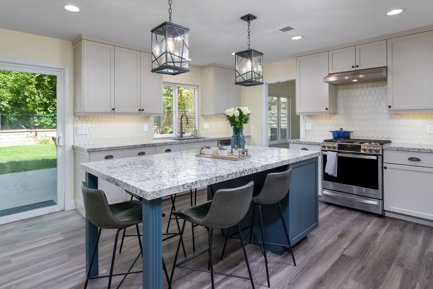 Modern white kitchen with marble island, gray floors, pendant lights, and stainless steel appliances