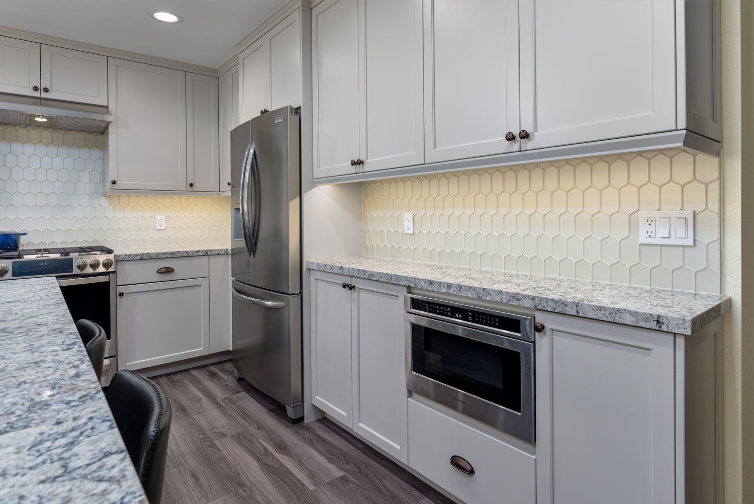 Modern gray kitchen with white cabinets, stainless steel appliances, and a speckled granite countertop