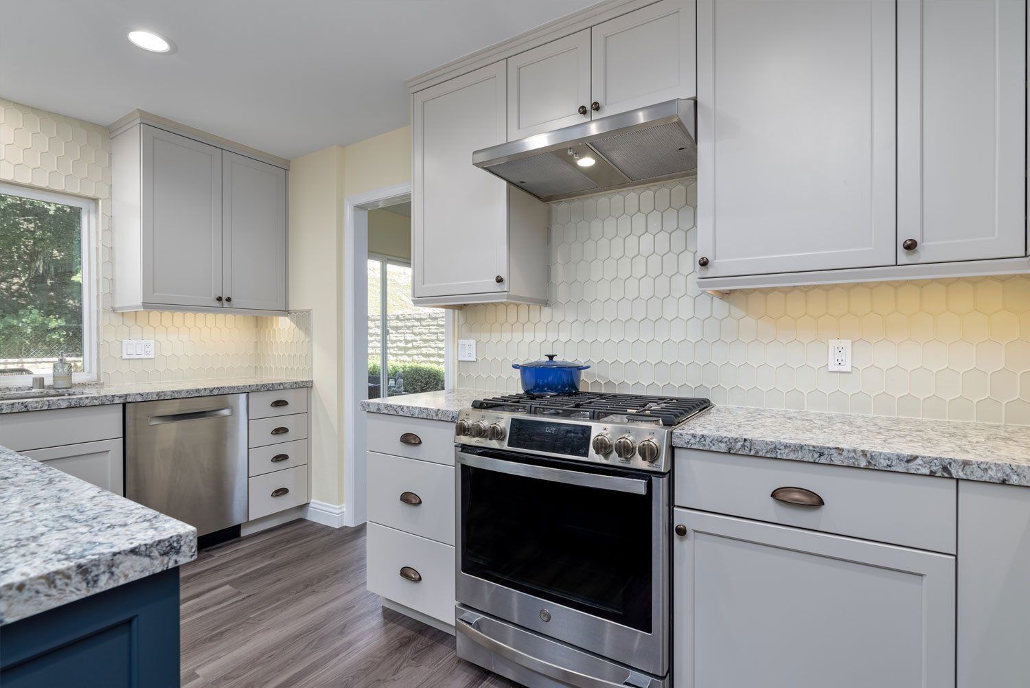 Modern kitchen with gray cabinets, stainless stove, granite counters, and tile backsplash