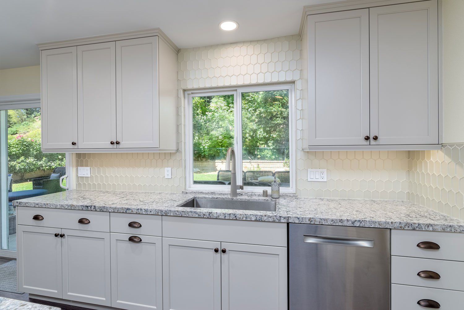 Bright kitchen with white cabinets, granite countertops, stainless dishwasher, and window over sink