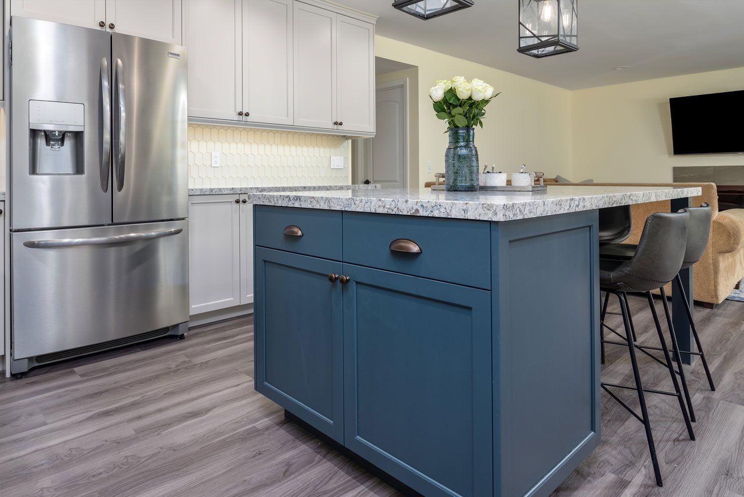 Modern kitchen with stainless steel fridge, blue island, white cabinets, and barstools
