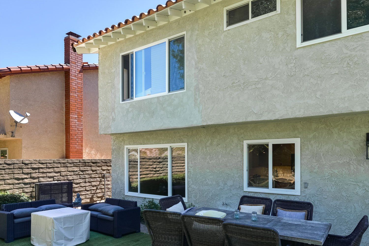 Backyard patio with wicker seating, stone wall, and a stucco house with windows and a balcony