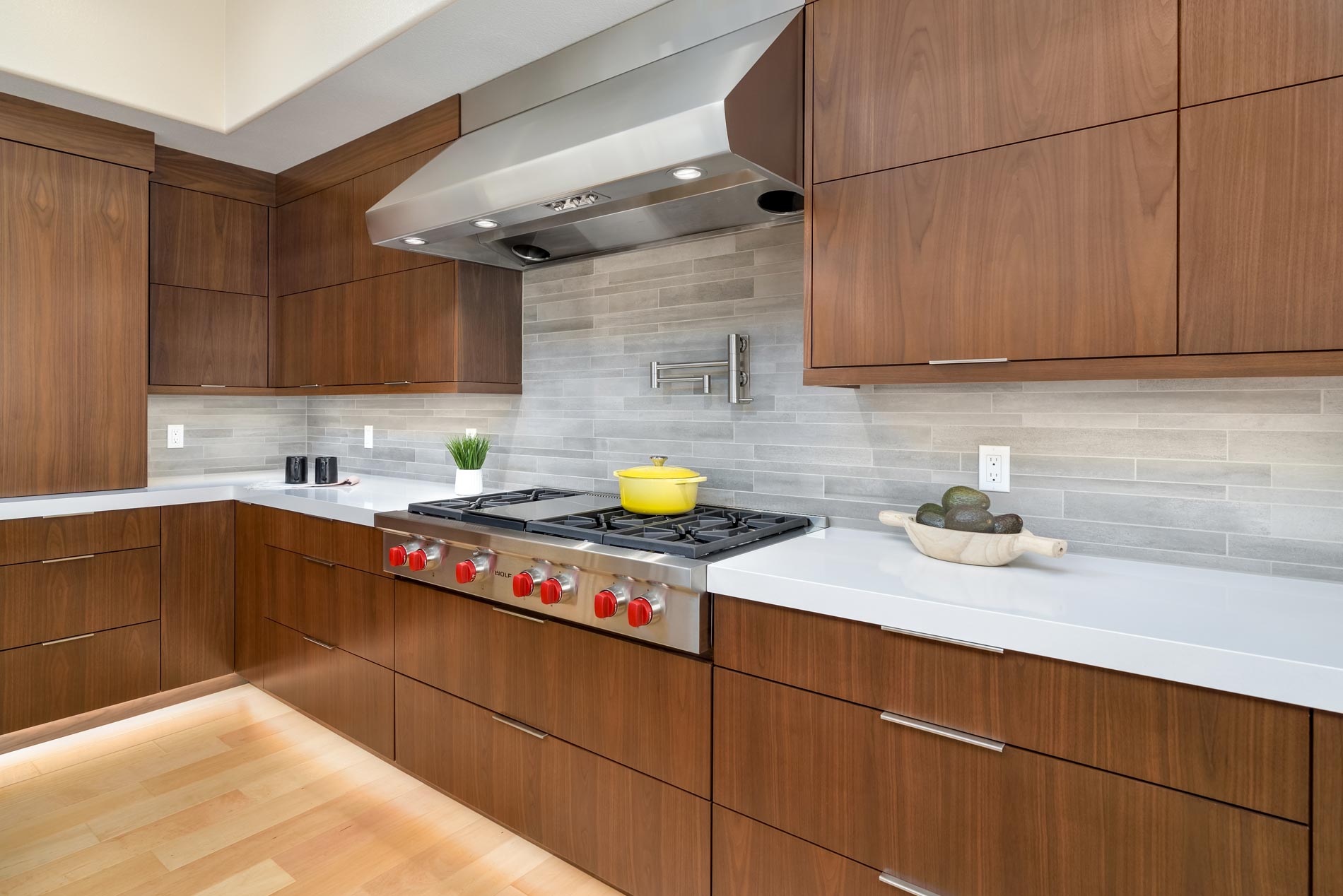 Modern kitchen with wood cabinets, white countertops, stainless range hood, and a yellow kettle on the stove