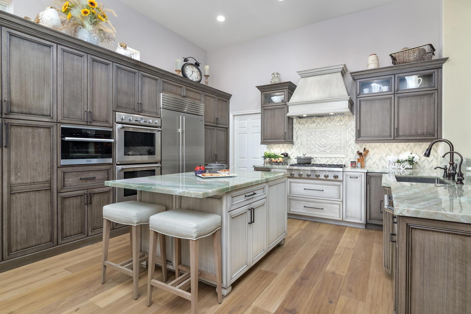 Bright modern kitchen with gray cabinets, white island, wood floors, and stainless appliances.