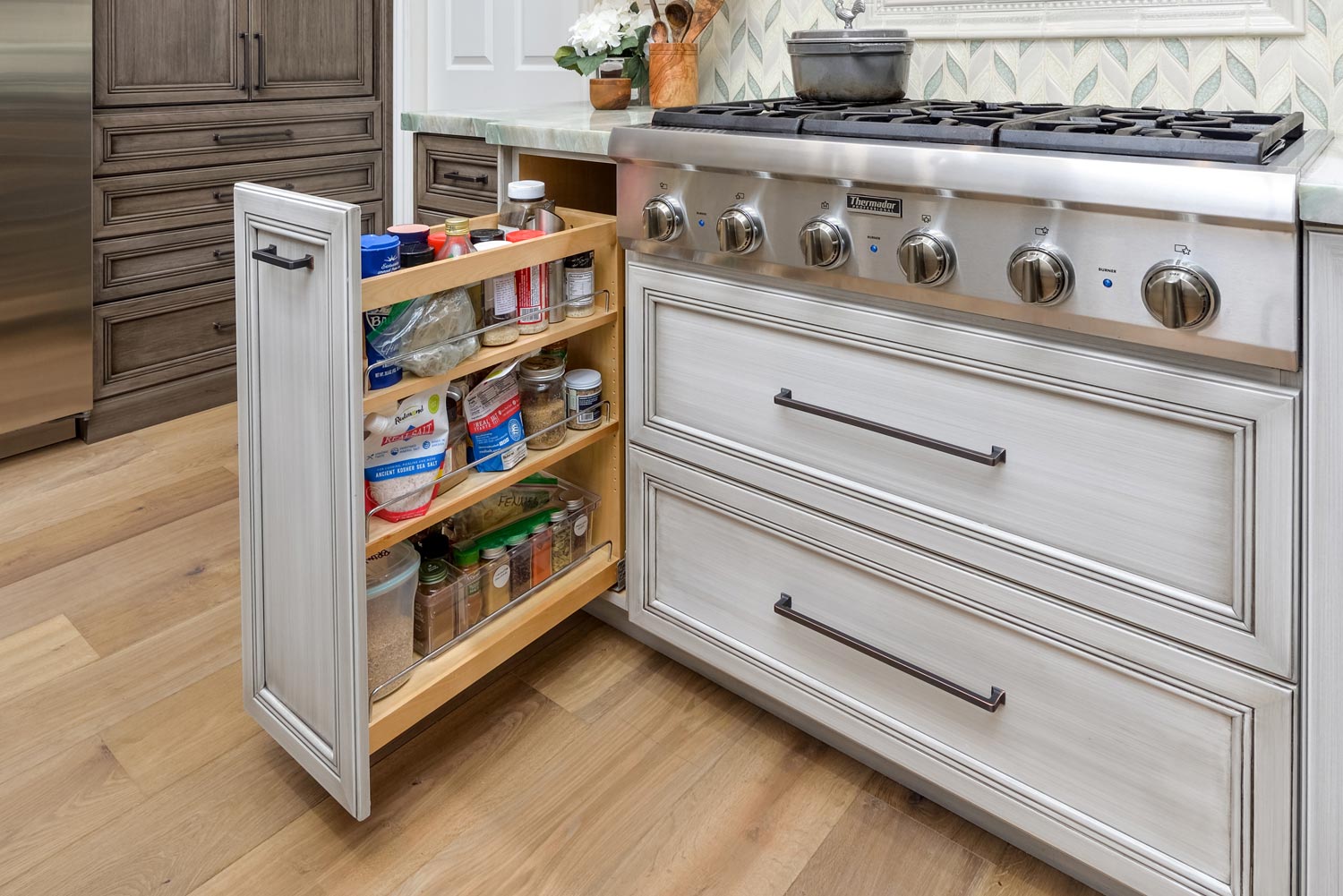 Open pantry cabinet beside a stainless steel stove in a bright kitchen.