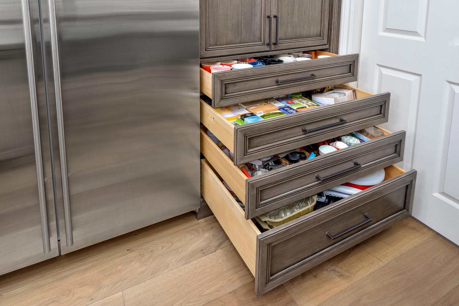Kitchen pull-out drawers with organized items next to a stainless steel refrigerator
